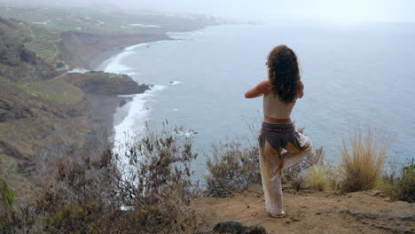 Against-the-backdrop-of-the-ocean,-beach,-and-rock-mountains,-a-woman's-yoga-warrior-pose-encapsulates-motivation,-inspiration,-and-a-dedication-to-maintaining-a-fit-and-balanced-life